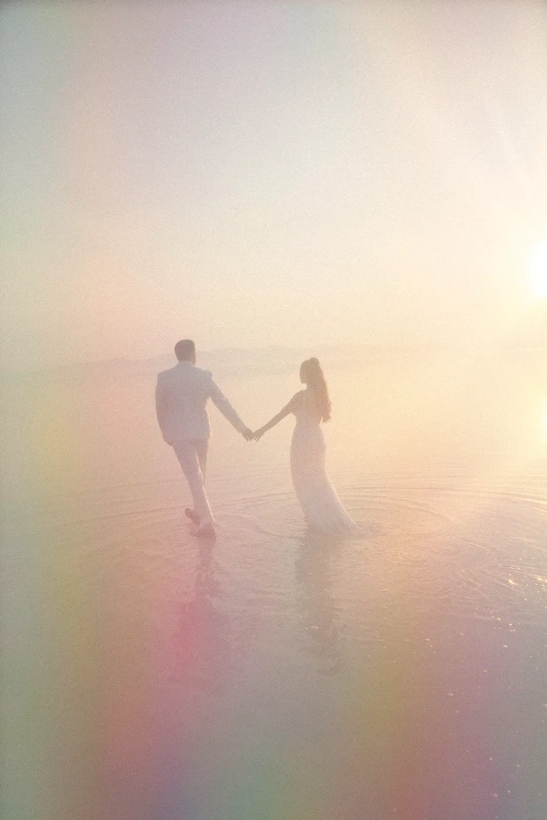Couple in wedding attire walks hand-in-hand through shallow water at sunset, surrounded by soft pastel hues from the Cara Mia Aurora preset, creating a romantic, ethereal atmosphere.